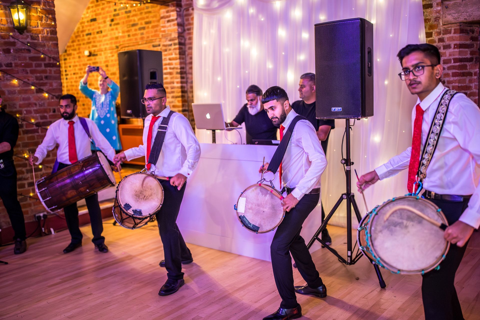 Dhol players dressed in white shirts black trousers standing and playing dhol drums