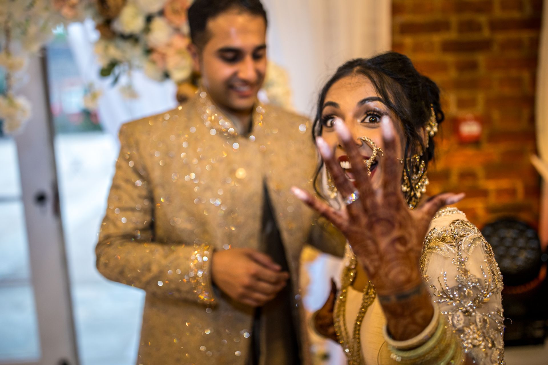multicultual wedding in traditional indian dress smiling to camera as the bride shows her henna hand