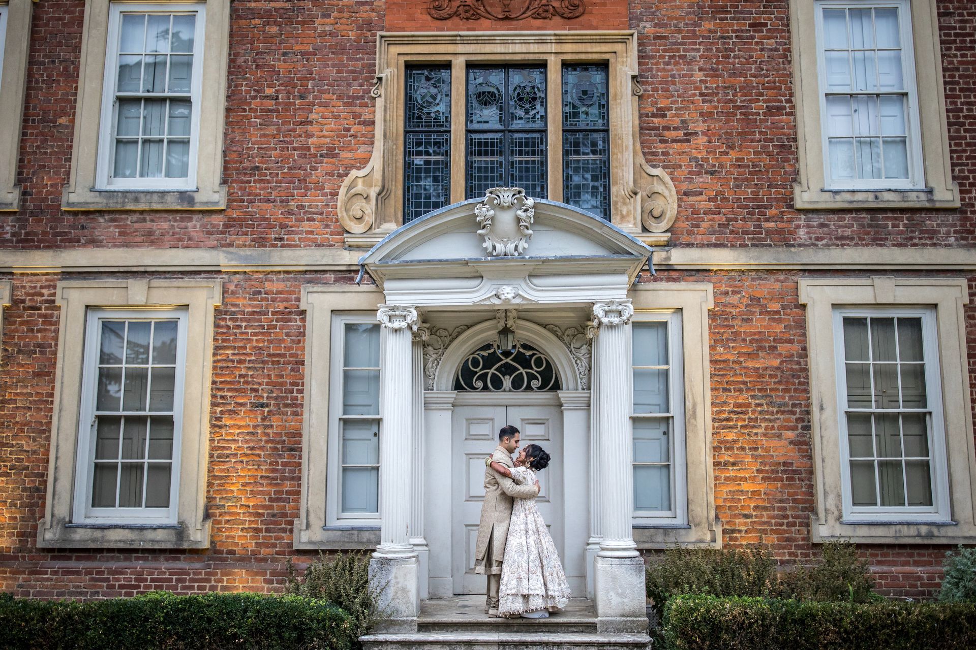 Indian bride and groom in traditional dress hugging each other outside Forty Hall