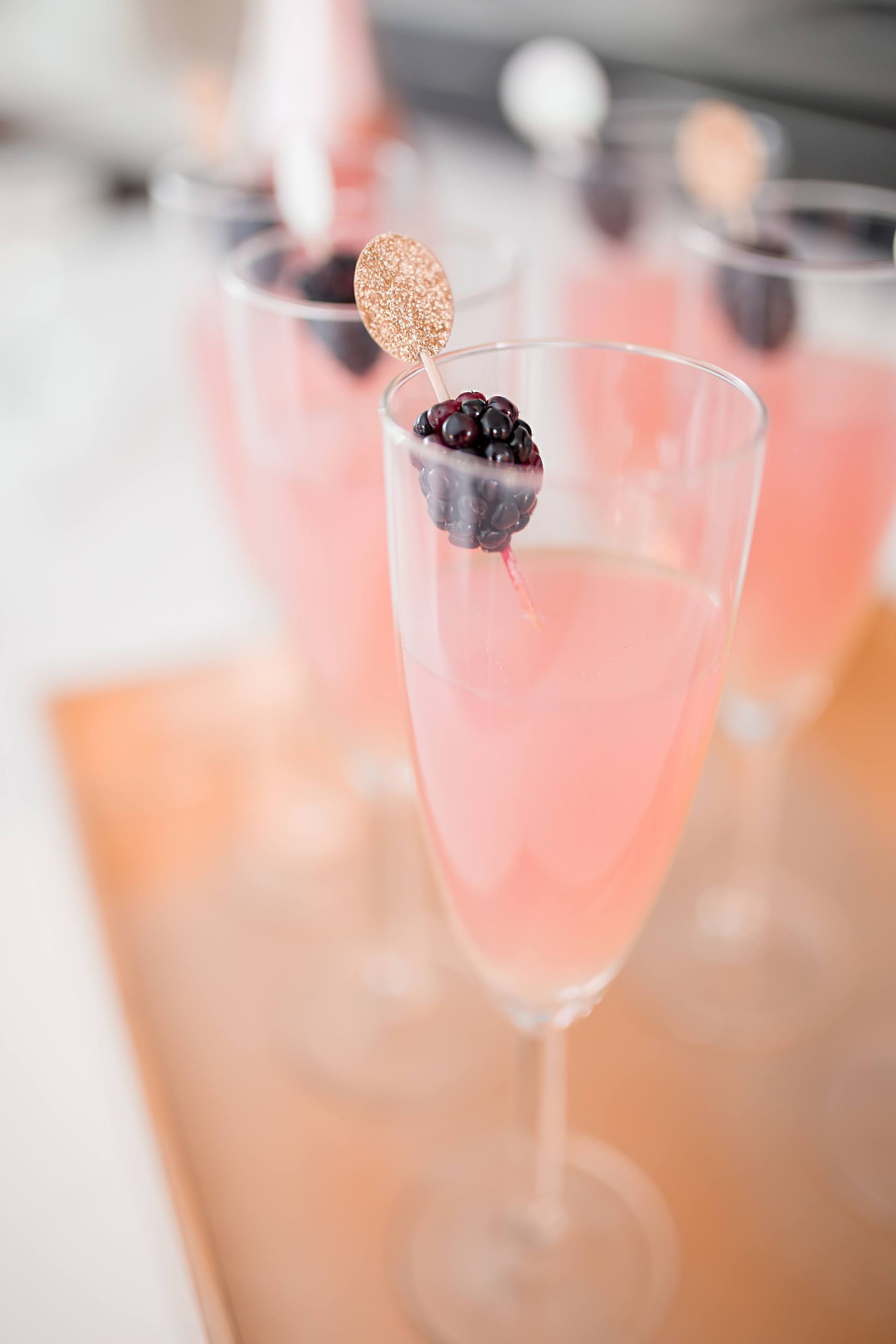 A trio of peach cocktail in a champagne glass garnished with blackberries