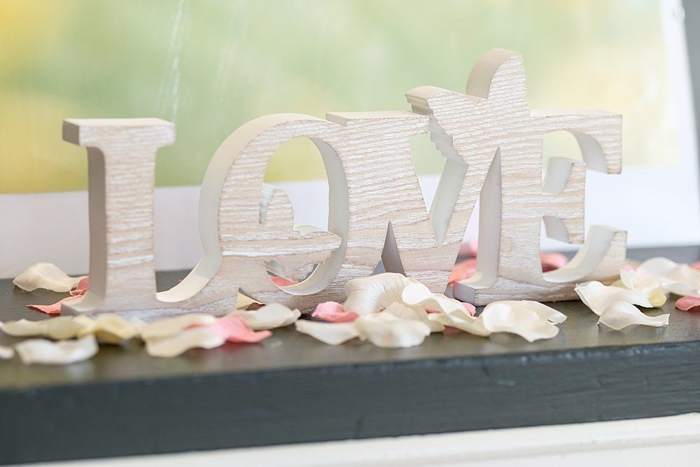 The word love is written in wood and surrounded by white and pink rose petals
