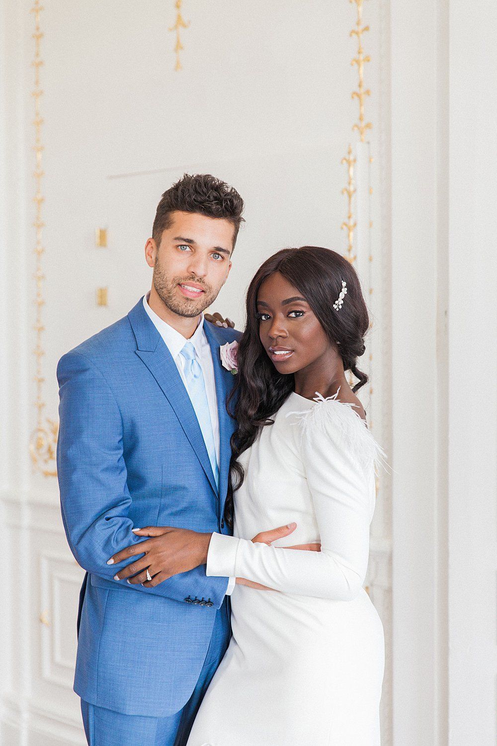 Image by Maxeen Kim Photography black bride in white dress and white groom in blue suit standing with arms around each other and smiling at camera