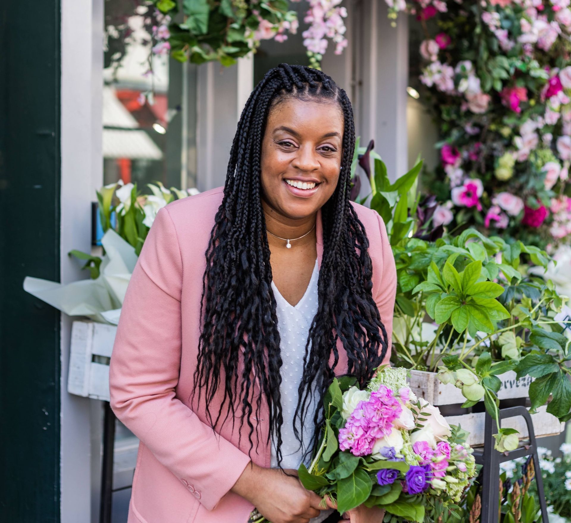 Black woman smiling at camera dressed in peach jacket and holding flowers