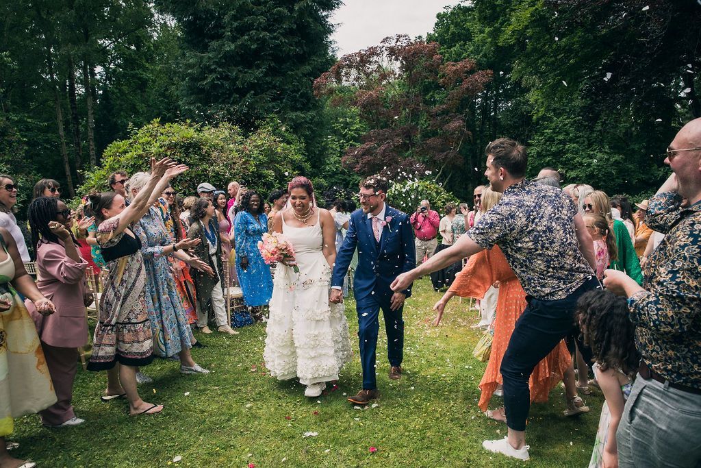 Bride and Groom holding hands walking up garden aisle as wedding guests throw confetti