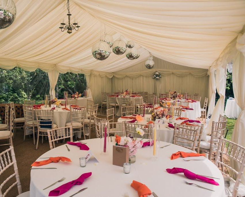 Colourful marquee wedding reception with pink and yellow flowers and pink and orange napkins by Pearline events