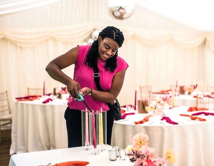 Pink and yellow candles surrounded by glass candle sleeve been lit on at table with pink flowers