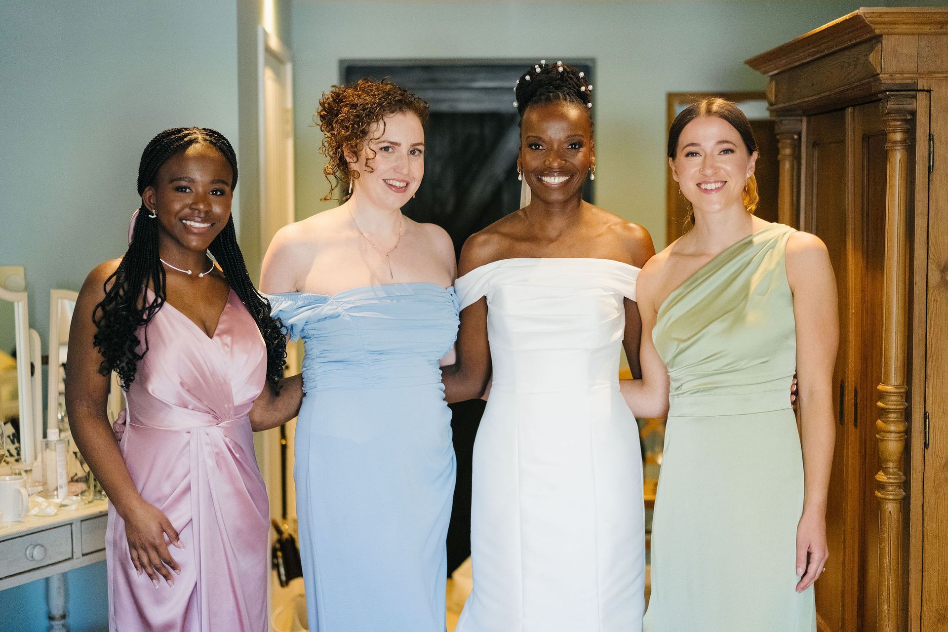 4 bridesmaids in pale pink, green and light blue bridesmaids' dresses standing with black bride all smiling at the camera