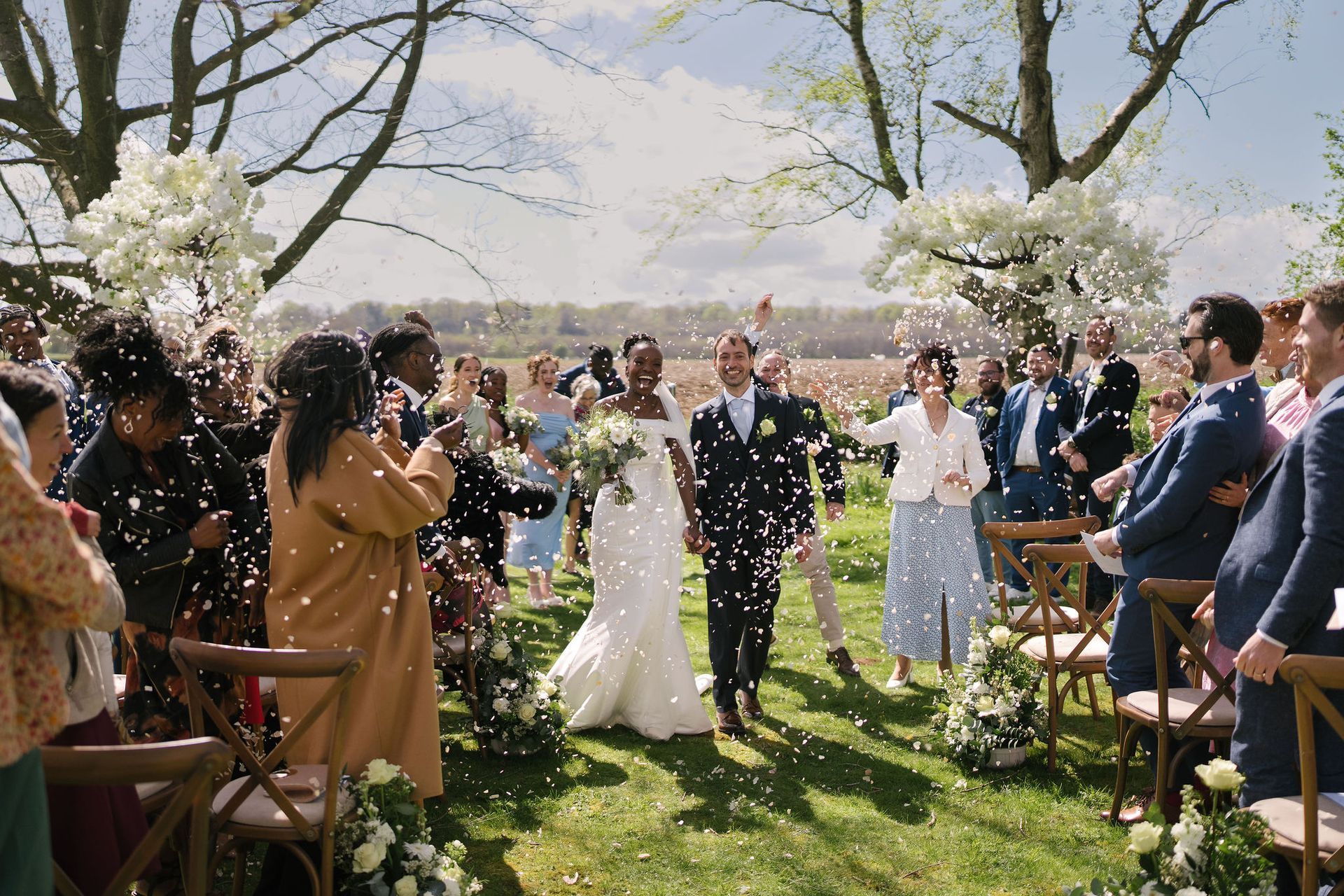 Bride and groom just married smiling and walking down their outdoor aisle holding hands as guests throw confetti at them