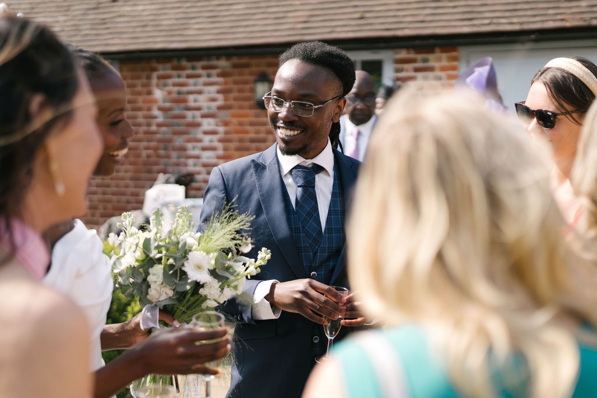 black man in blue suit smiling taking to other wedding guests outside