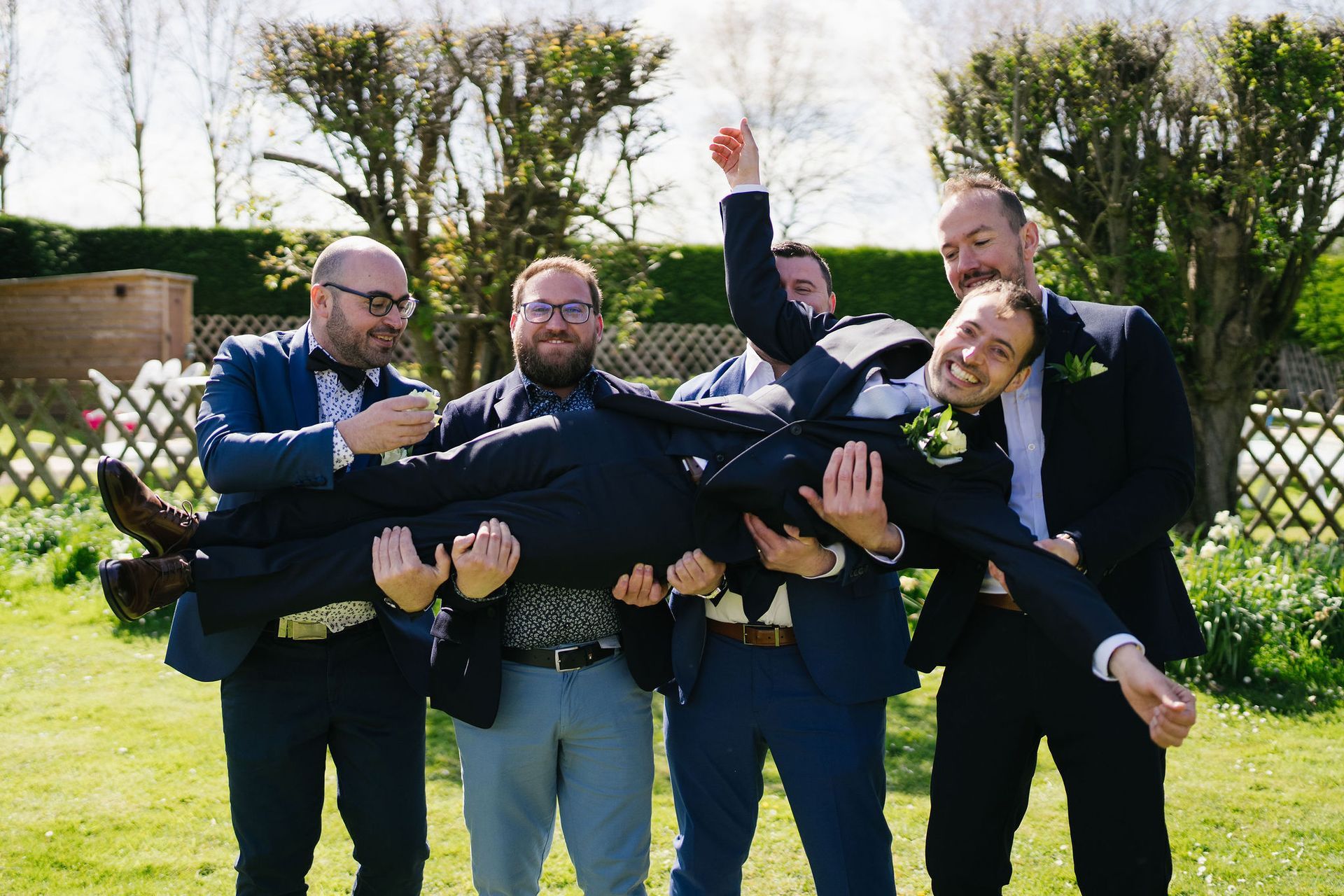 Groom in a blue suit been held horizontally by 5 groomsmen outside