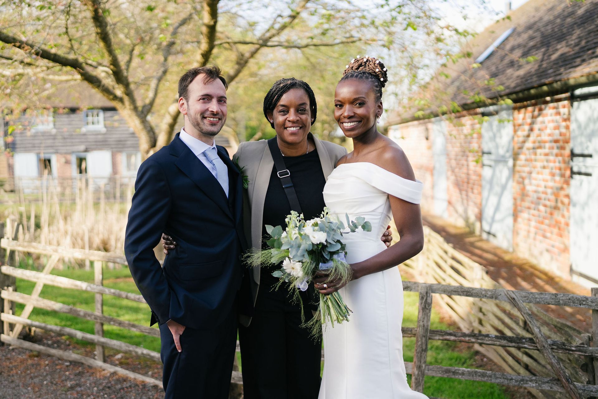 bride and groom standing either side of their wedding planner, outside smiling at the camera