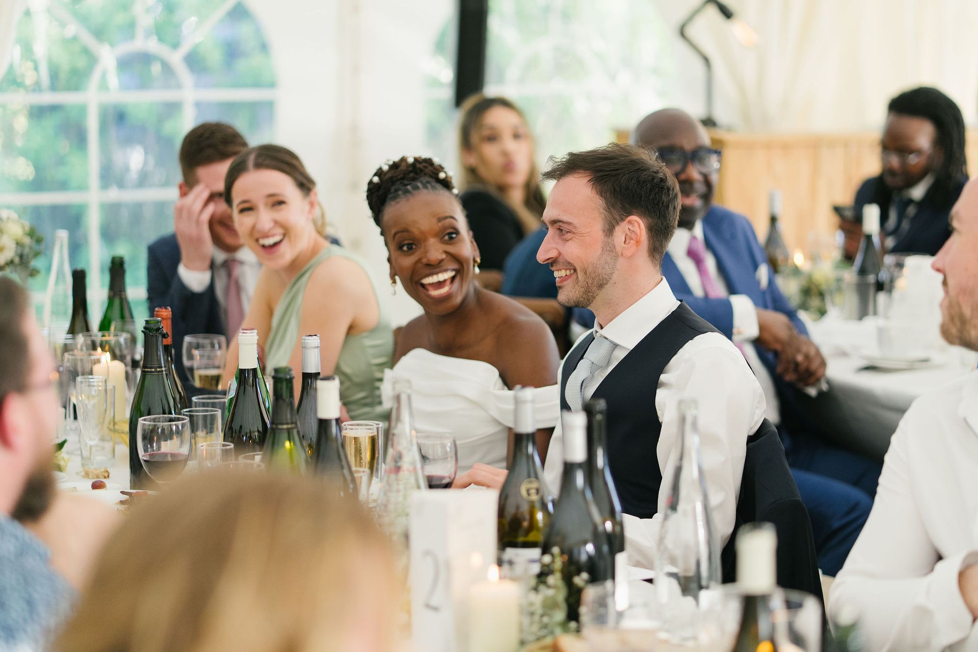Bride and groom seated and smiling with wine bottles on the table
