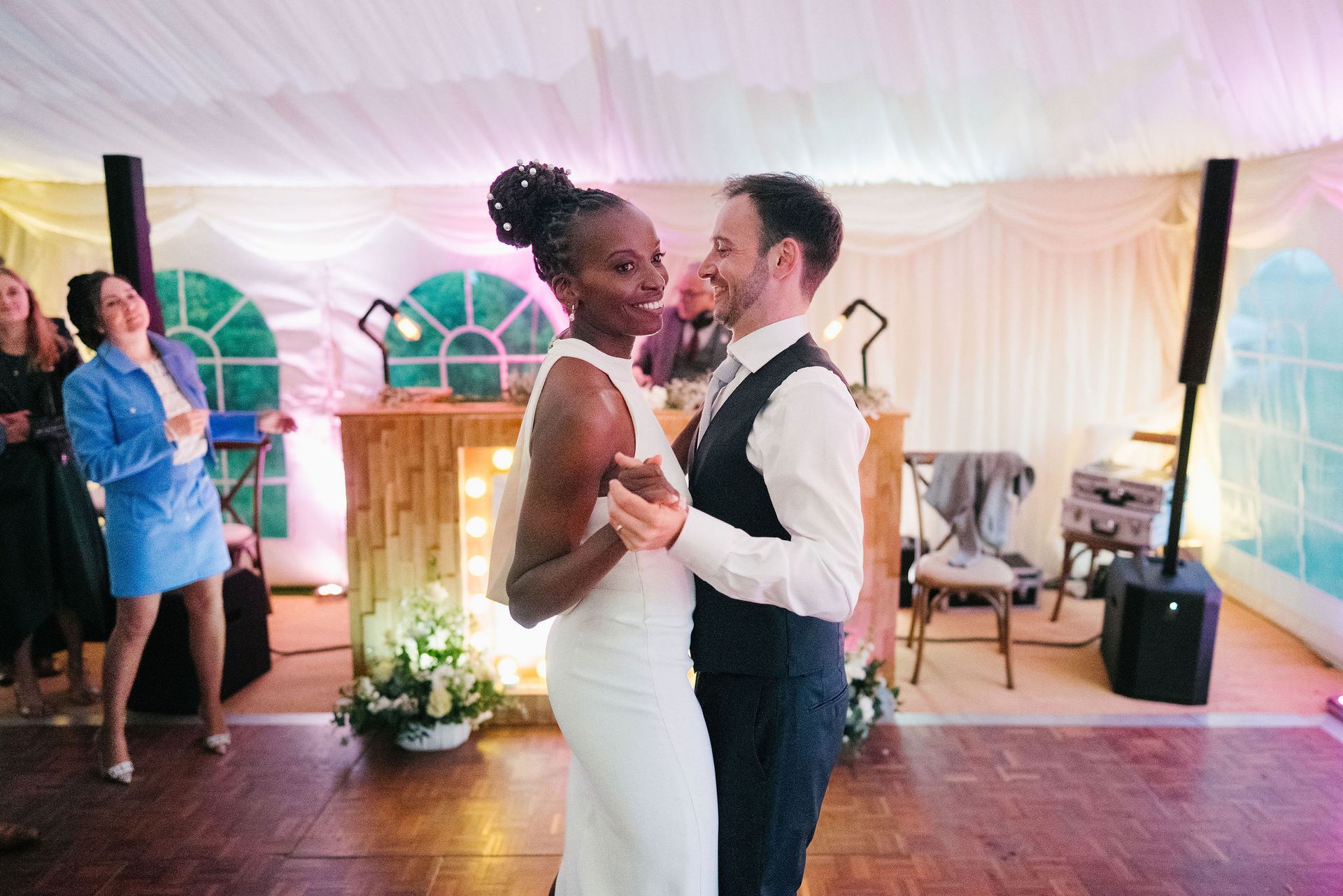 black bride and white groom holding hands whilst daning with DJ booth in the background