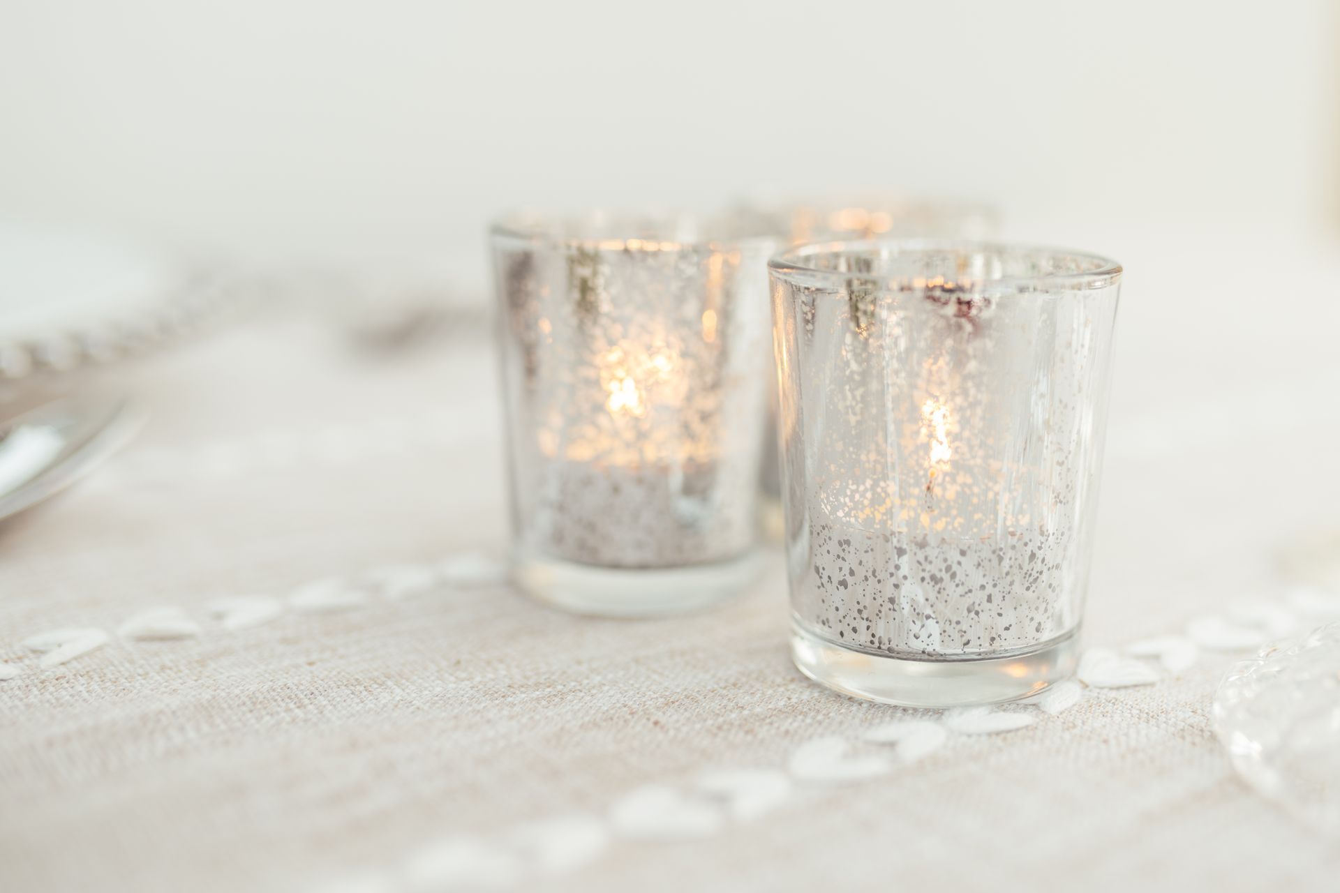 Three silver tea light holders displayed on table with beige tablecloth