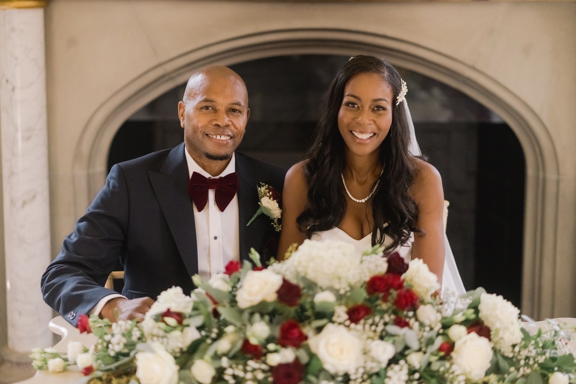 Black bride and groom sitting at a table with flowers smiling at the camera