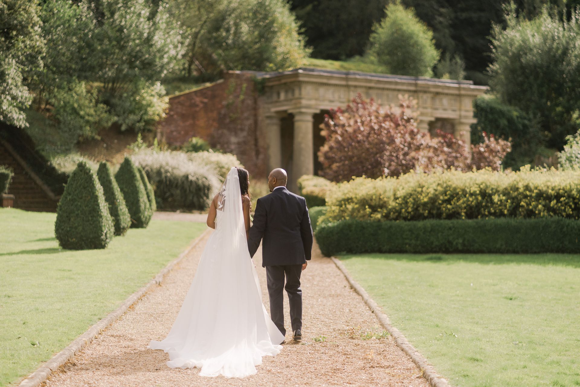 Black bride and groom with backs to camera walking up a path in the grounds of Wotton House Hotel Surrey