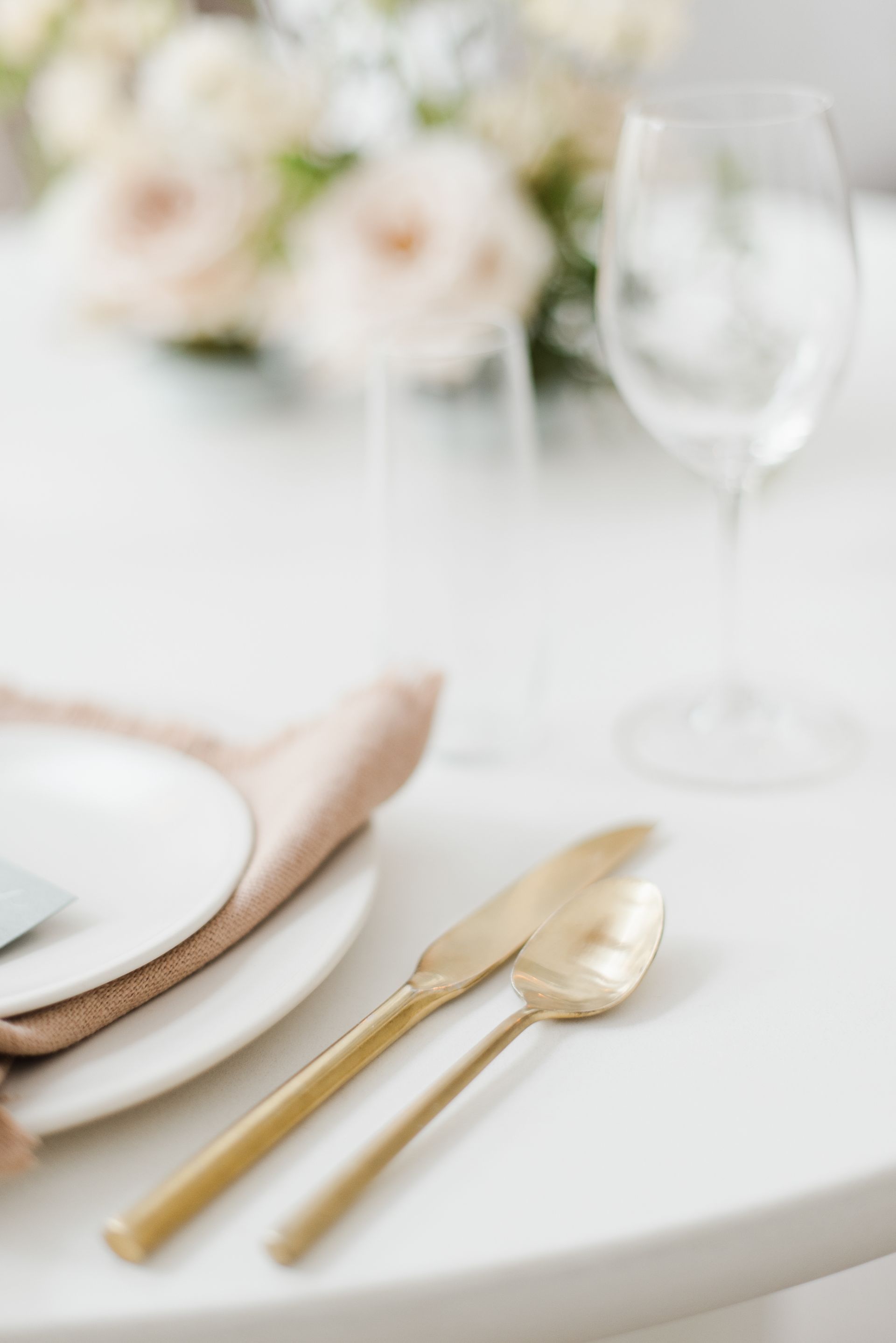 Gold cutlery and white plate on a table setting with a clear wine glass