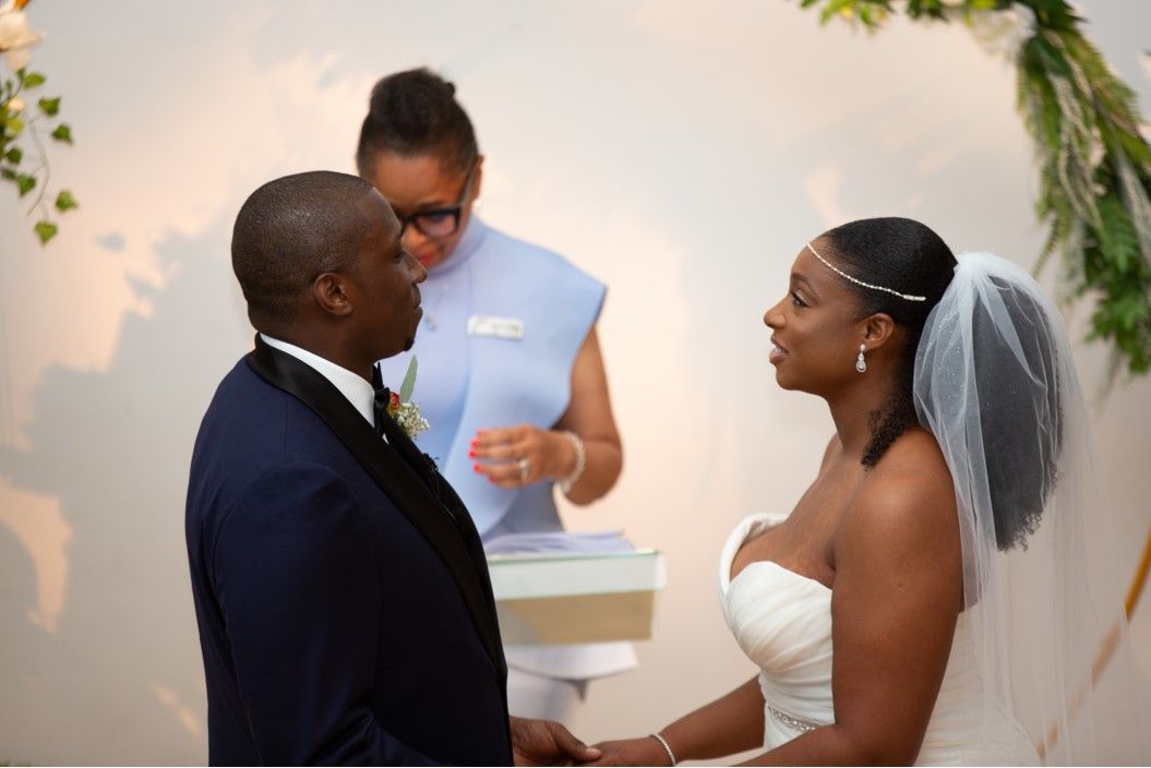 Black bride and groom facing each other with celebrant at wedding ceremon