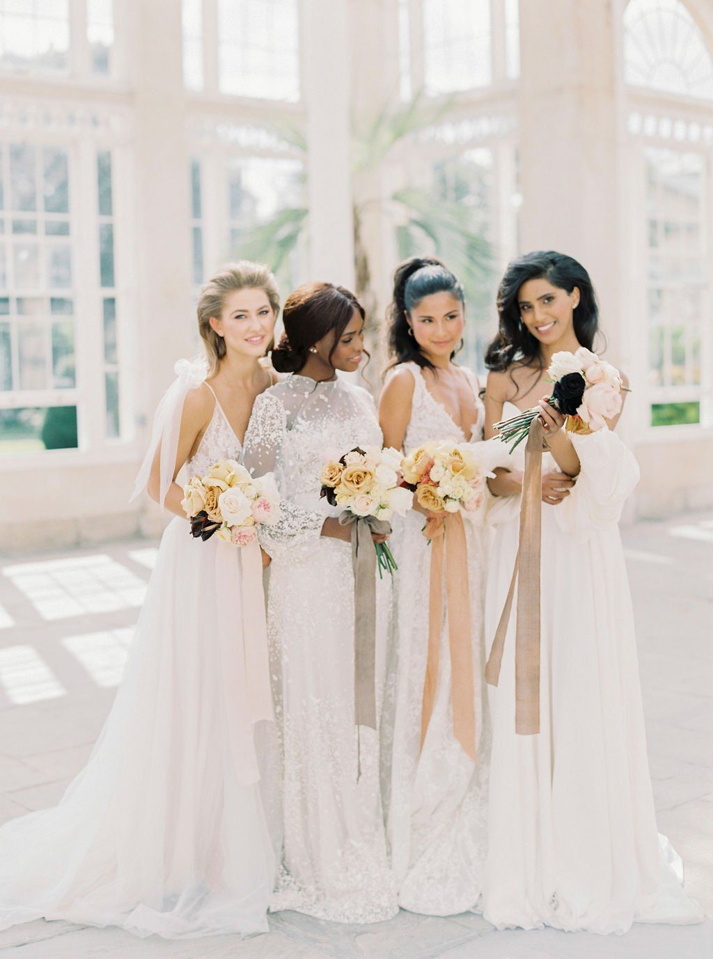 4 bridesmaids in white dresses all smiling and holding bouquets