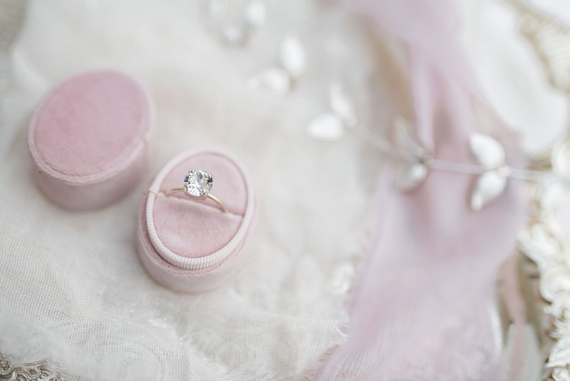 Close-up of a diamond engagement ring in a pink ring box with lace in the background