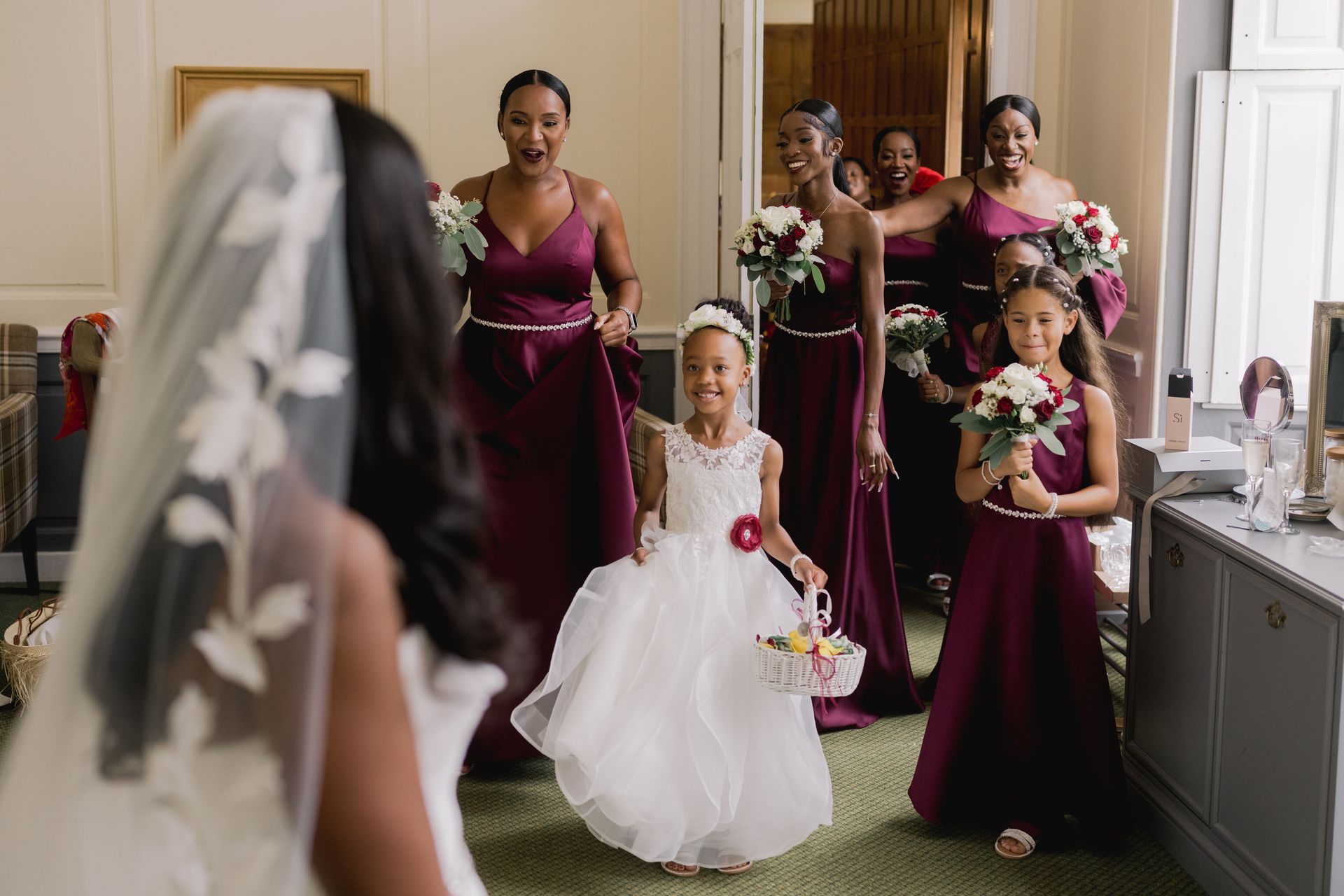 Group of bridesmaids in dark red dresses walking in to see the bride for the first time