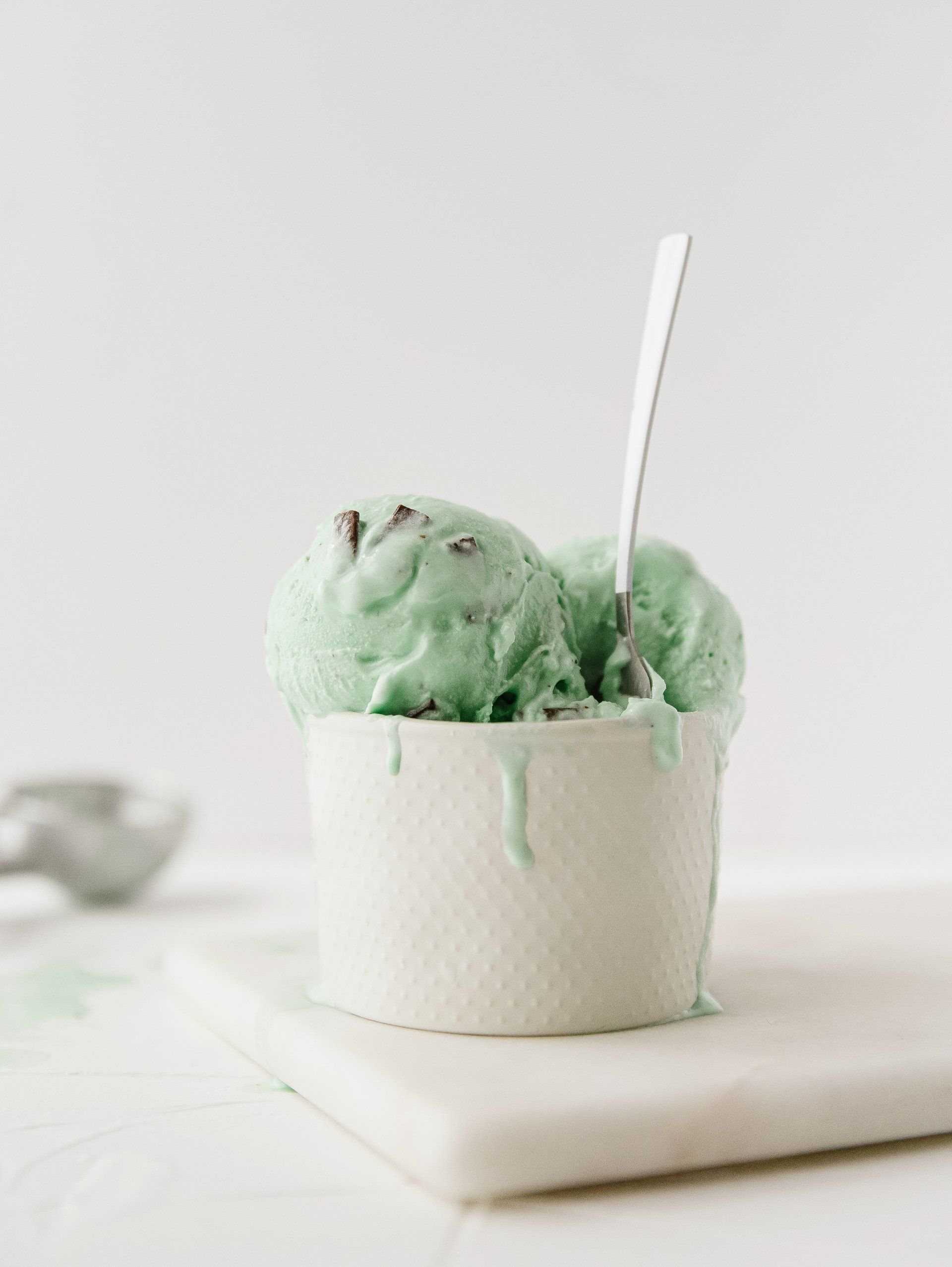 Scoops of mint chocolate ice cream in white bowl and silver spoon in the ice cream