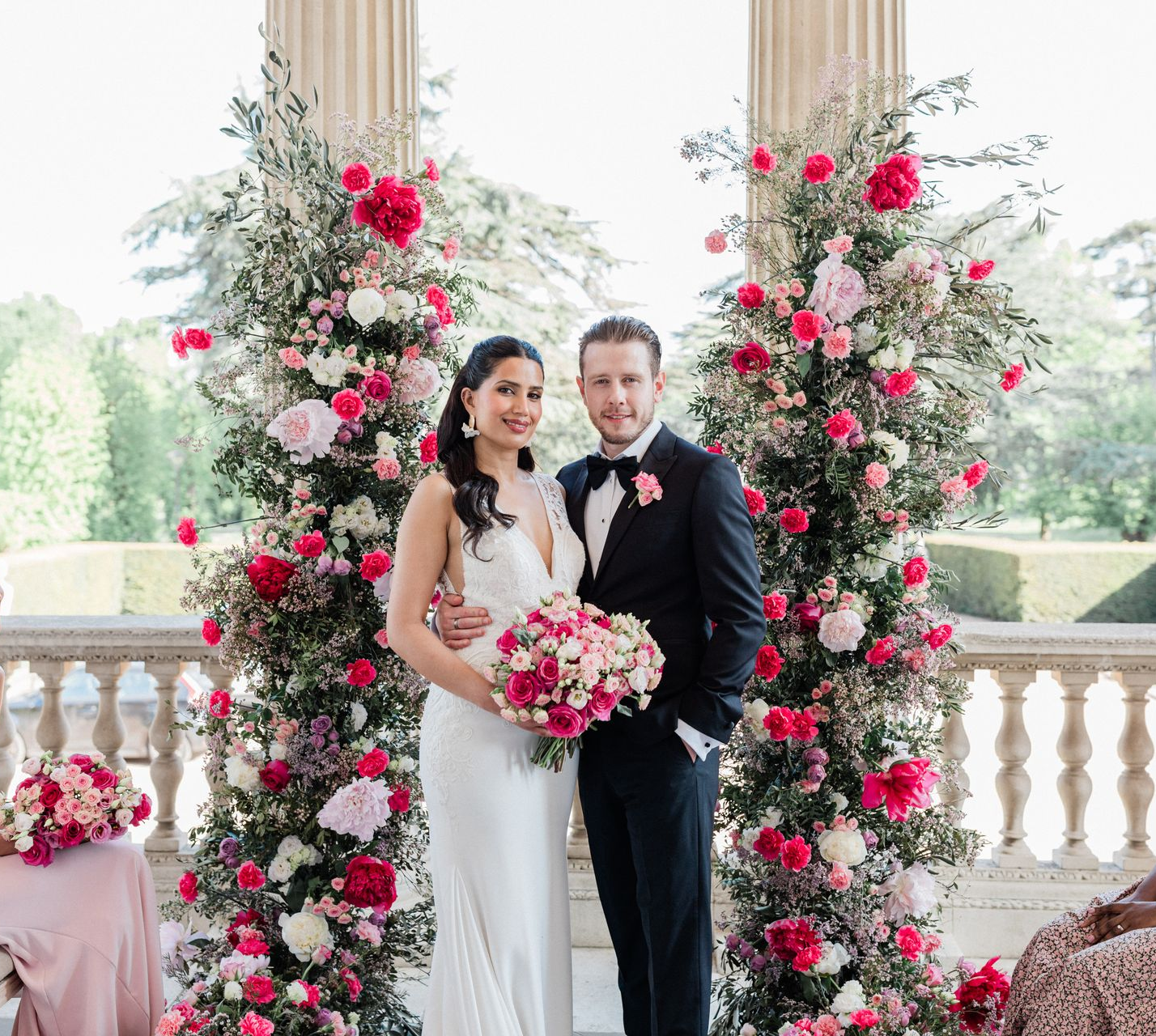 Bride and groom smiling by the wedding ceremony flower arch at colourful multicultural wedding in London, planned by Pearline Events