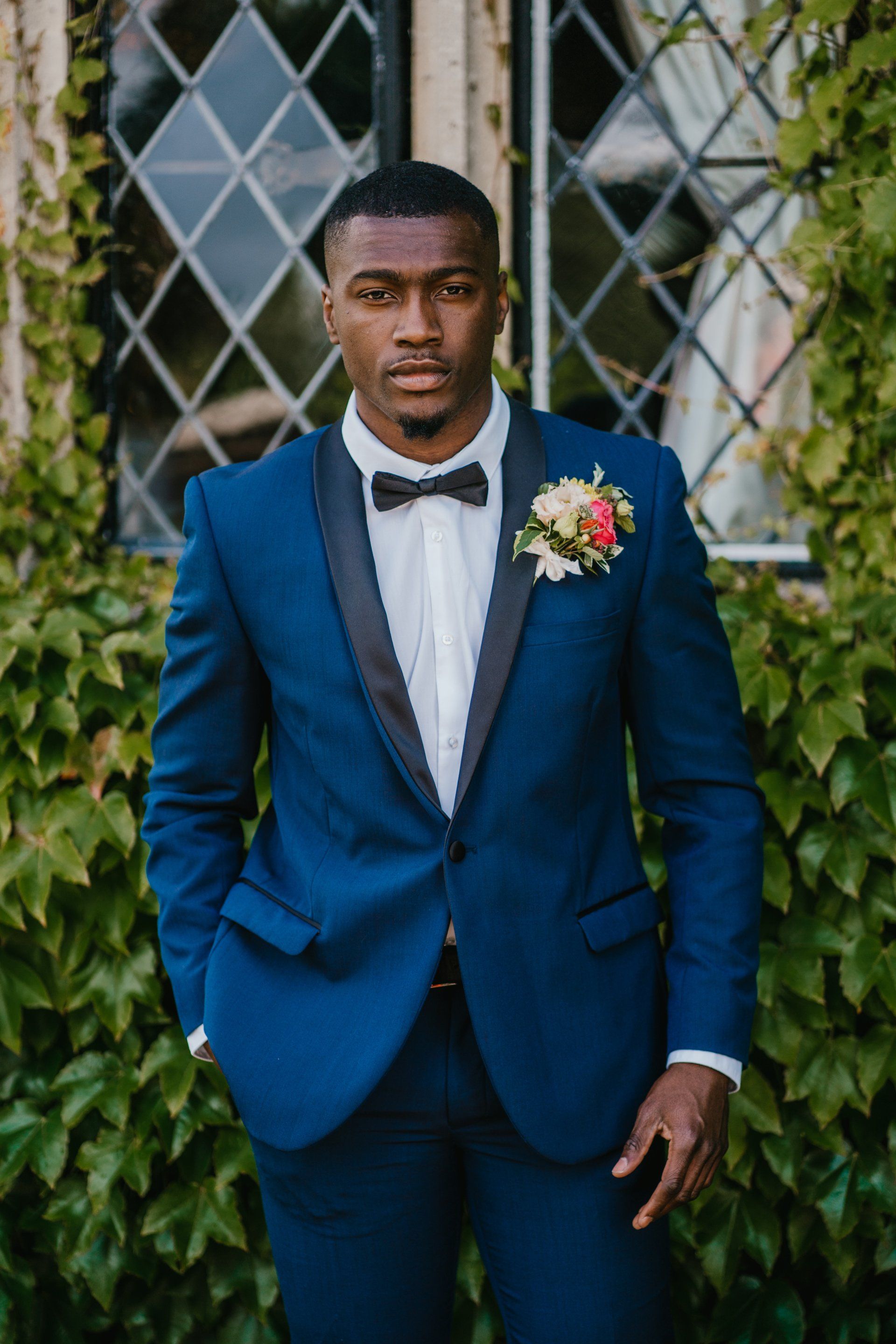 Black groom in blue tuxedo outside Eastwell Manor