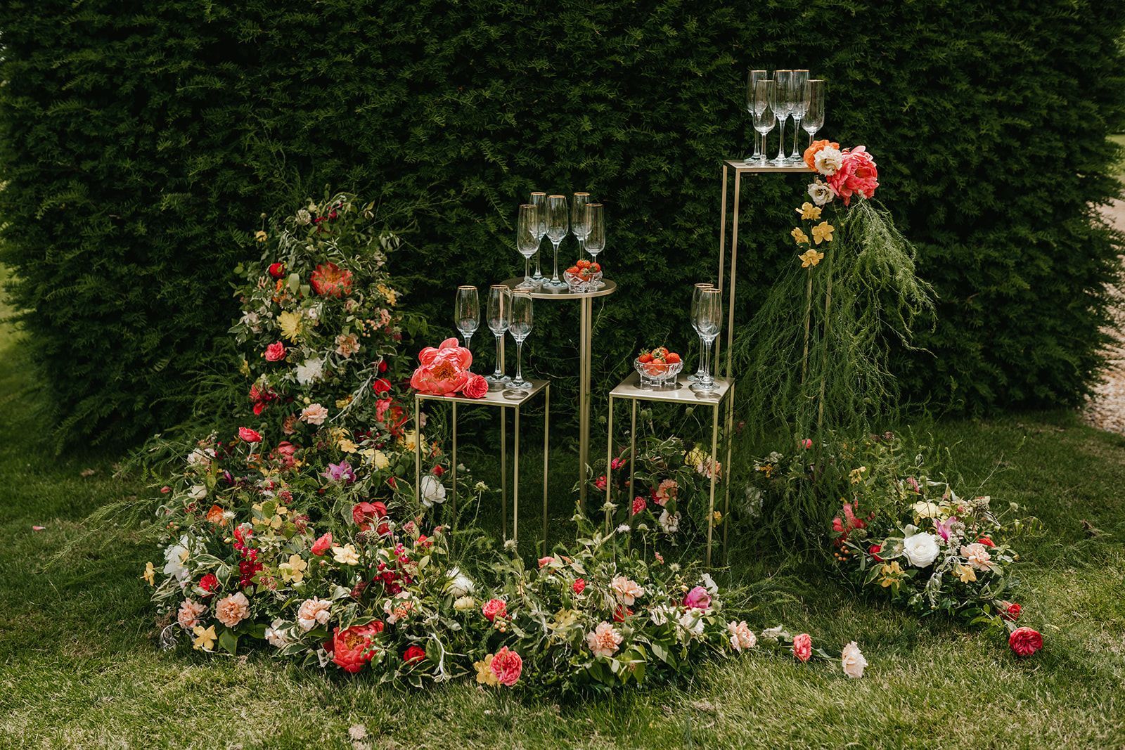 A group of champagne glasses displayed on gold pedestal's and surrounding by foliage and orange and peach flowers