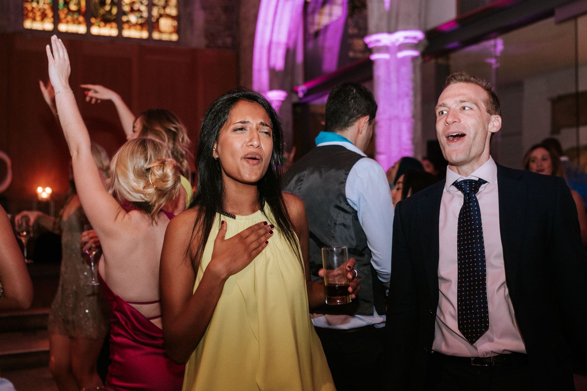 Asian woman in lime green dress holding a drink and dancing next to a white man in a blue suit smiling and dancing