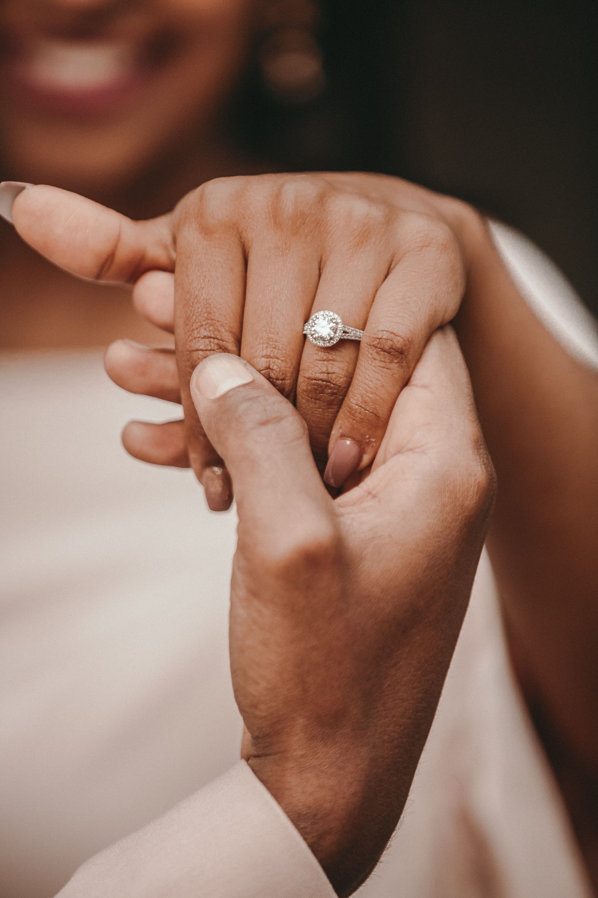 Close up of a black man holding the hand of a black woman who is wearing a round diamond engagement ring