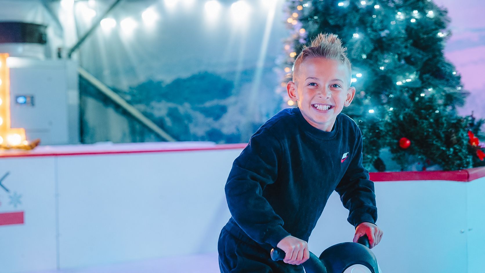 Young boy with huge smile using a skate aid on an ice rink