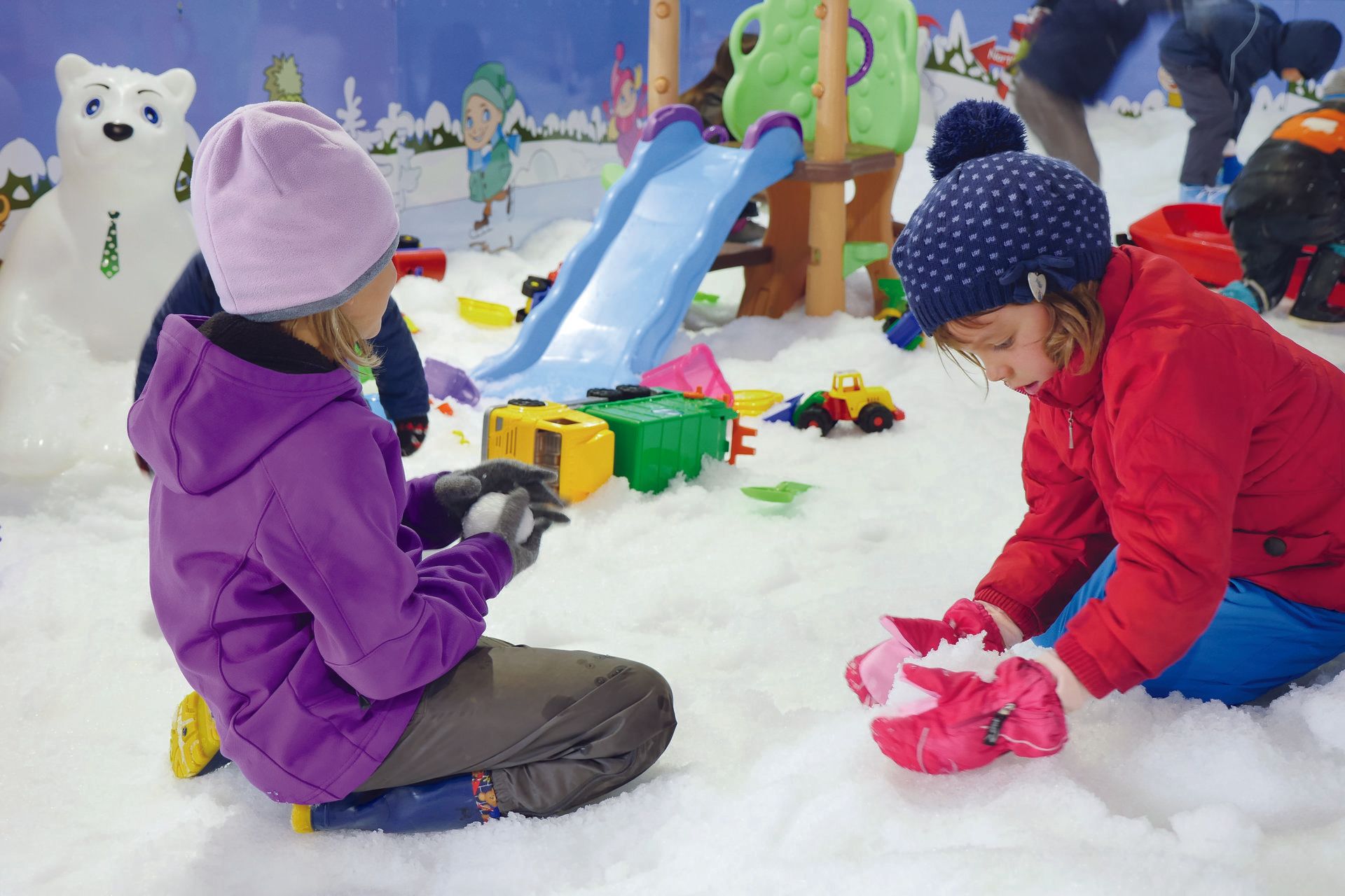 Children playing inside a Snow Playbox enclosure with a little slide and toys