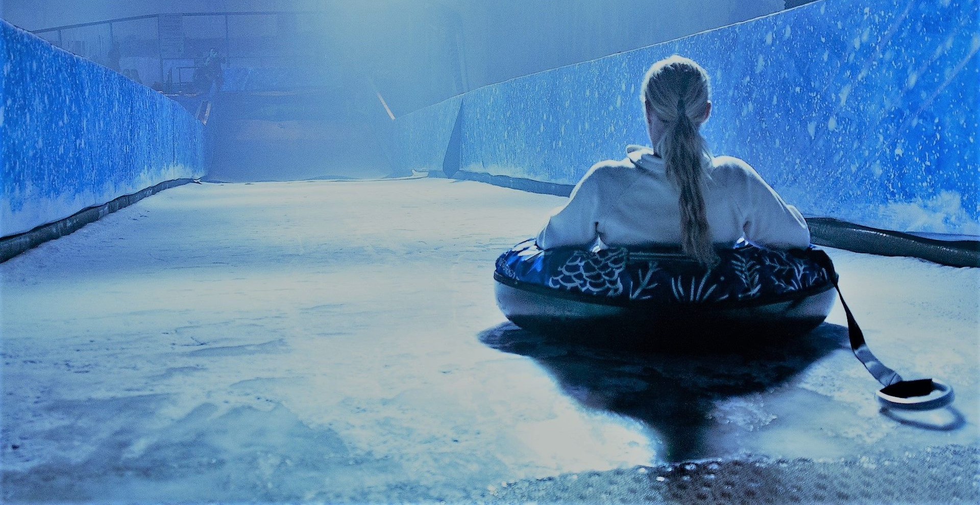 Photo from behind of a girl on an inflatable.  She is at the top of a large ice slide about to set off