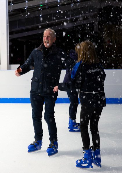 Two people on an ice rink wearing blue ice skates with falling snow and a big smile from the gentleman