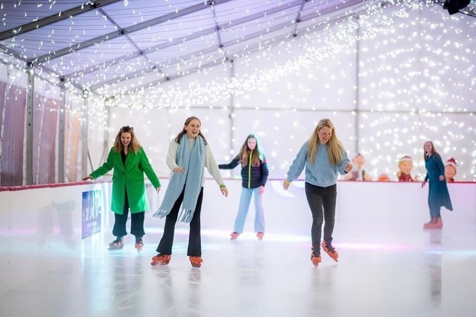 Four young girls ice skating wearing orange ice skates