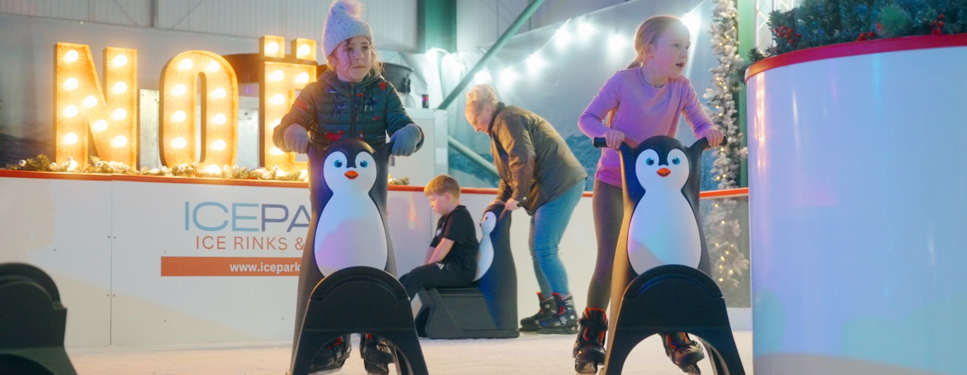 Two young children ice skating using very cute 'Polly' penguin skate aids