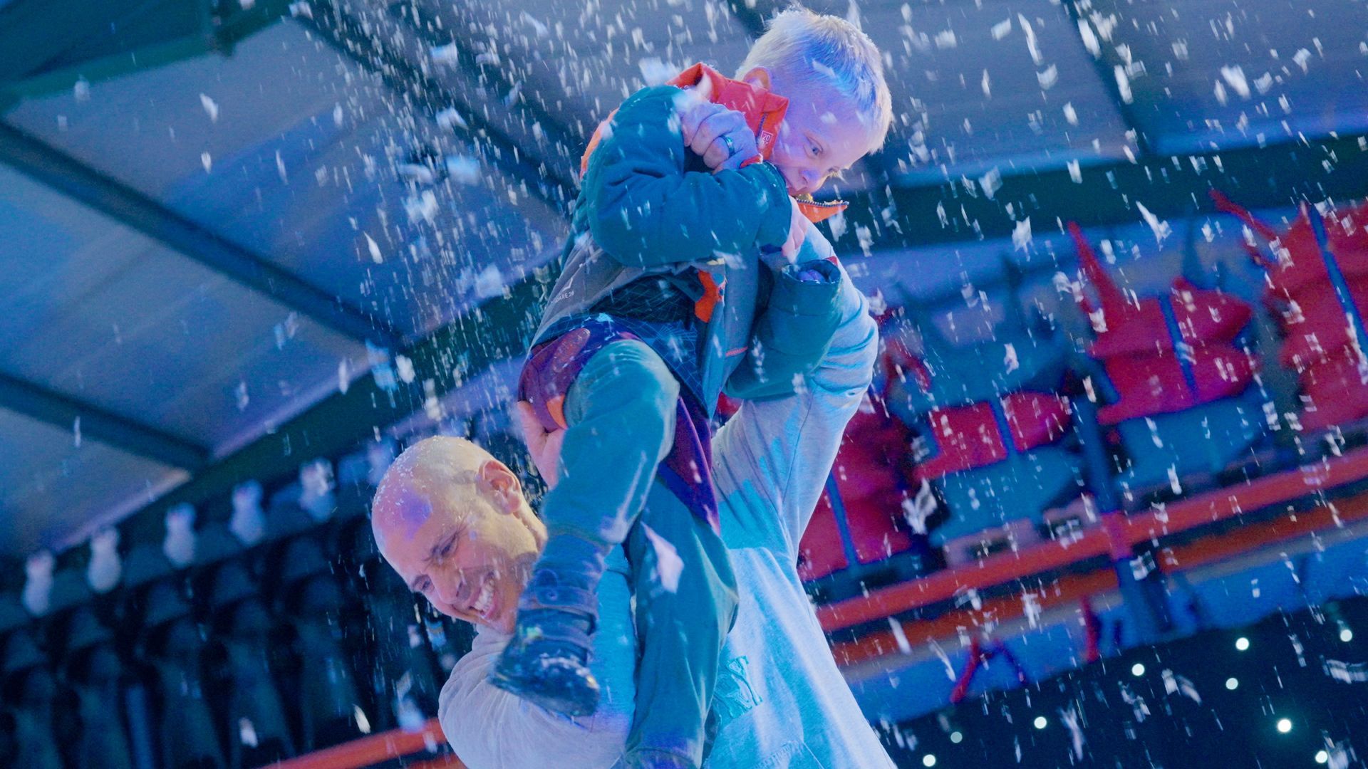 Dad lifting his son up above his head under the falling snow