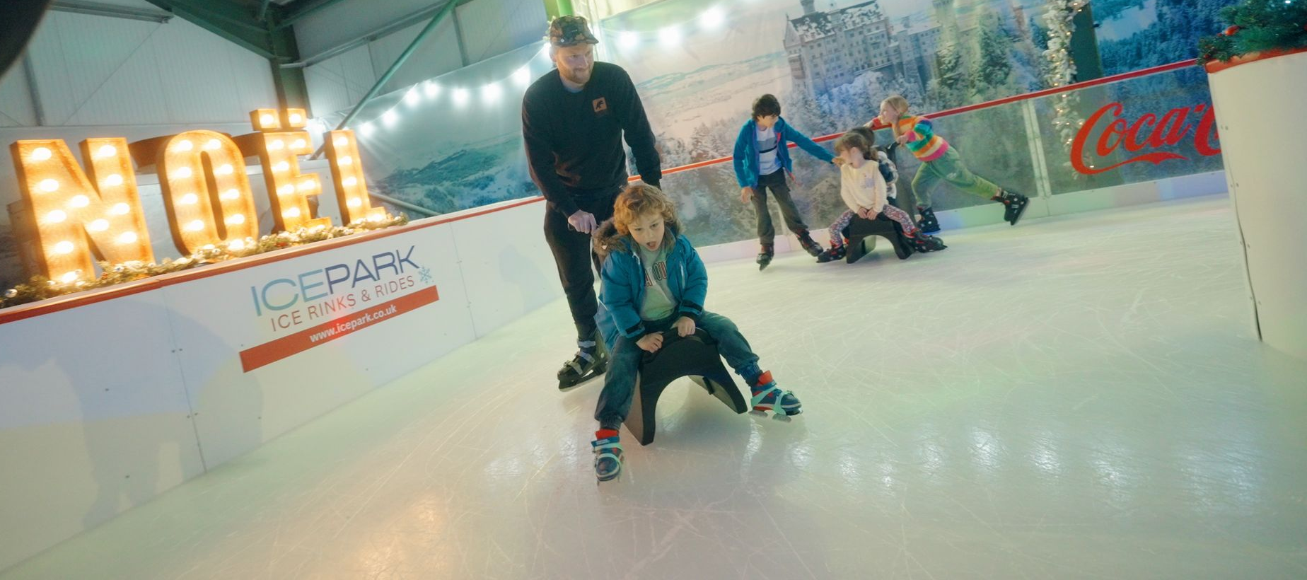 Ice rink with dad and young boy using Polly Penguin skate aid on Ice Park ice rink