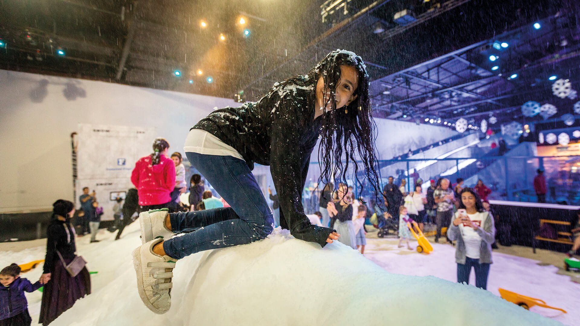 Girl on a huge pile of fresh snow. Wearing jeans and a huge smile.