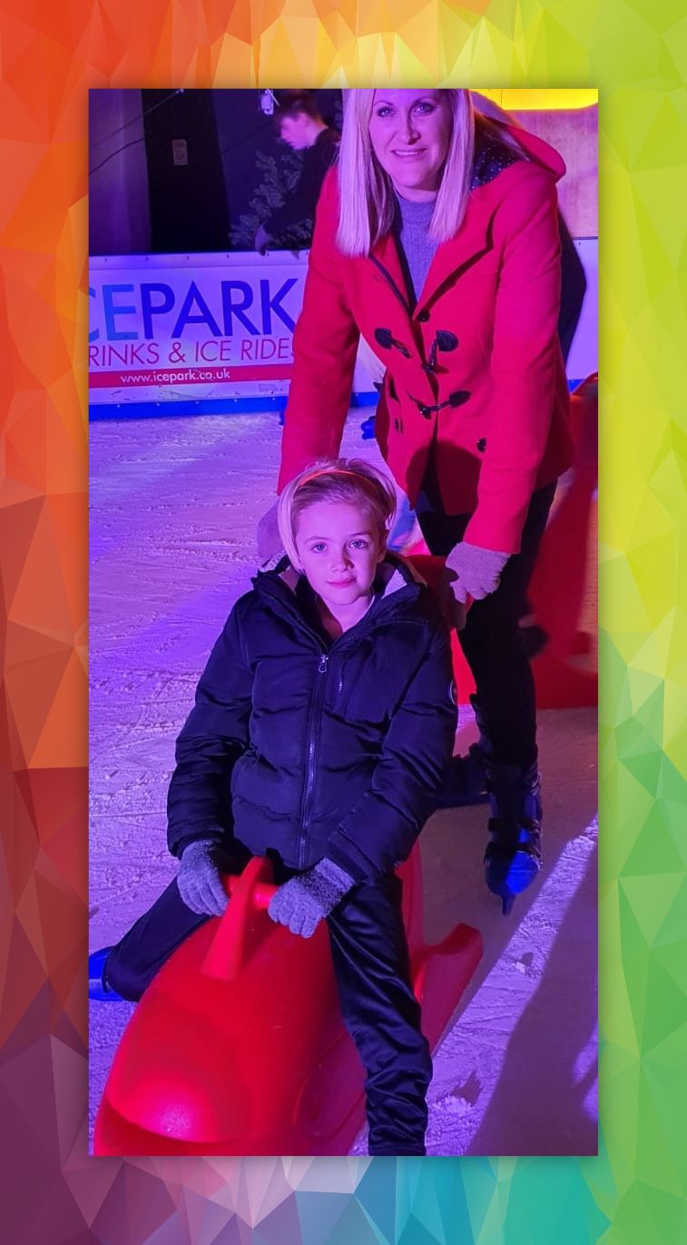 Youngster sitting on a red dolphin skate aid with mum in red winter coat pushing.