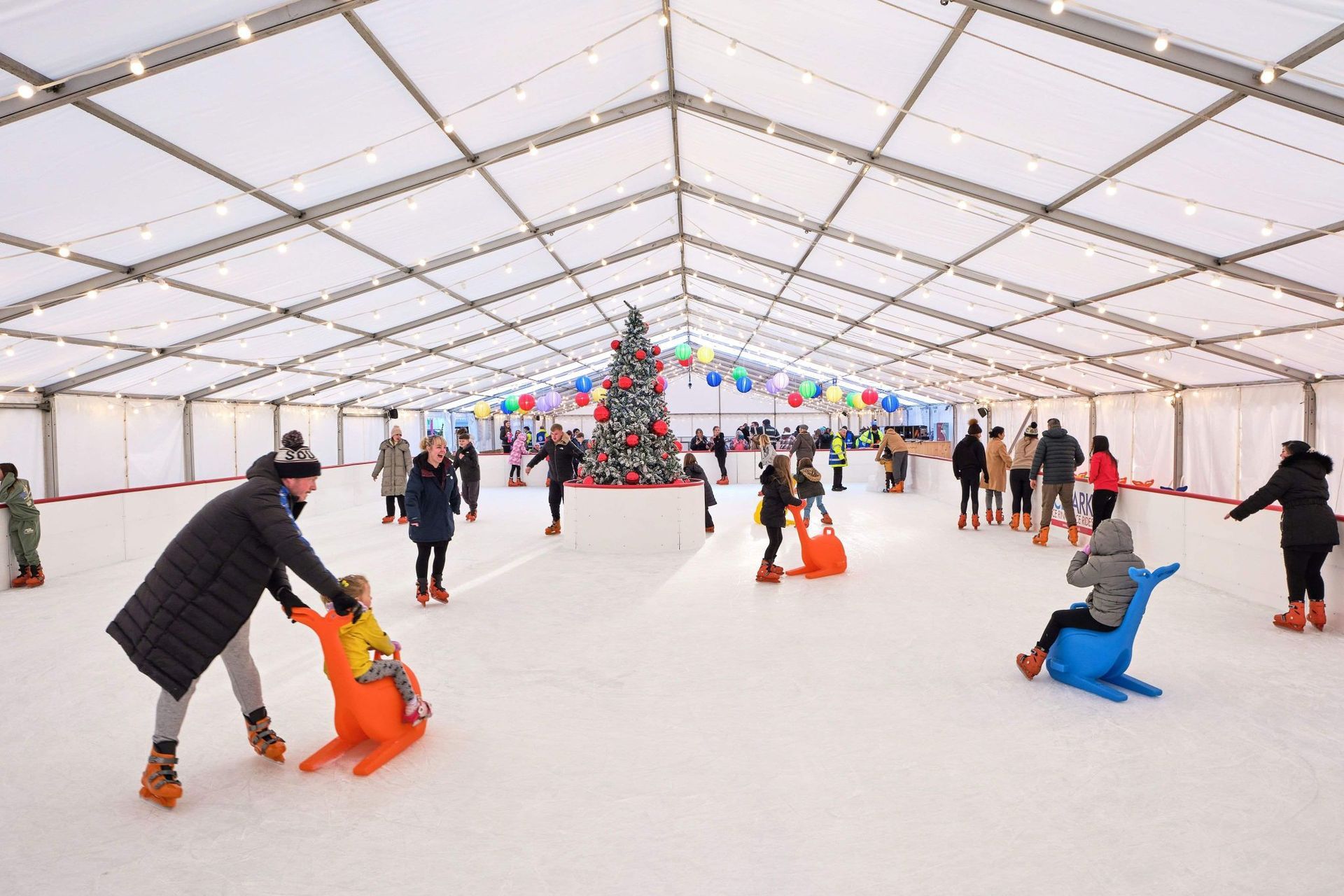 Full panoramic view of Christmas decorated ice rink with a large Christmas tree in the centre with large red bubals.
