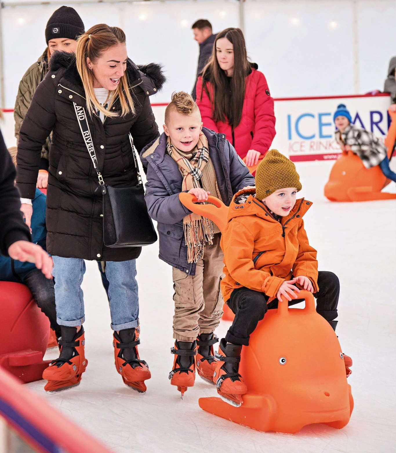 Mum and two young boys. One pushing a red dolphin skate aid the other sitting on the skate aid