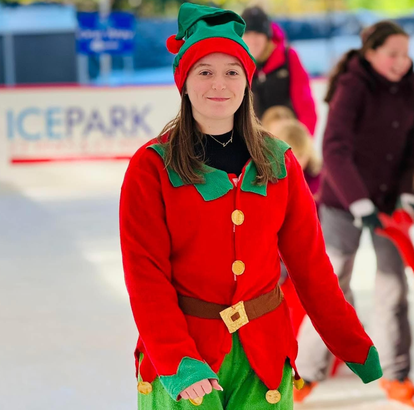 Beautiful girl dressed as an elf in red / green tunic and hat. ice skating