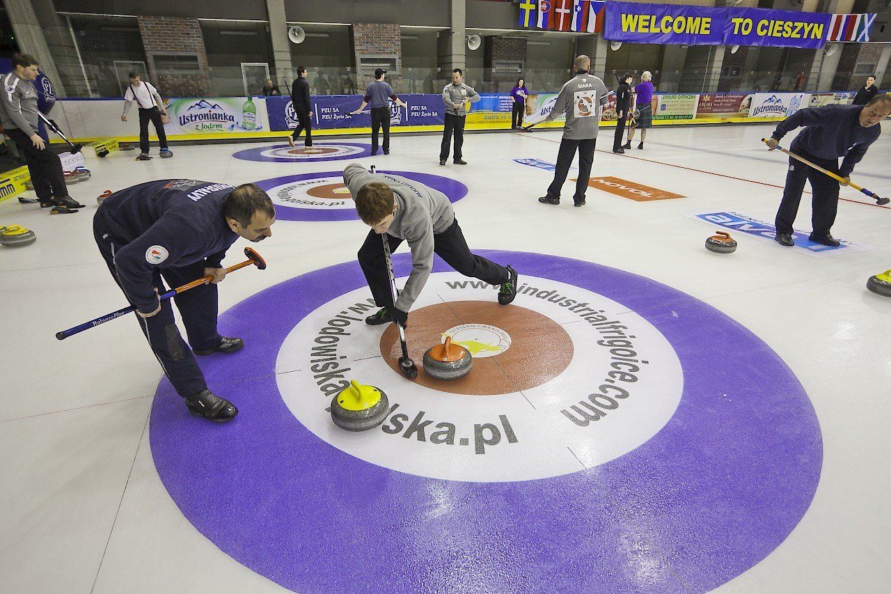 Full size curling ice rink with players sweeping the target