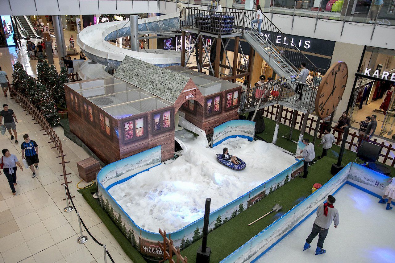 Children ice skating around the perimeter of a small slide in a shopping centre