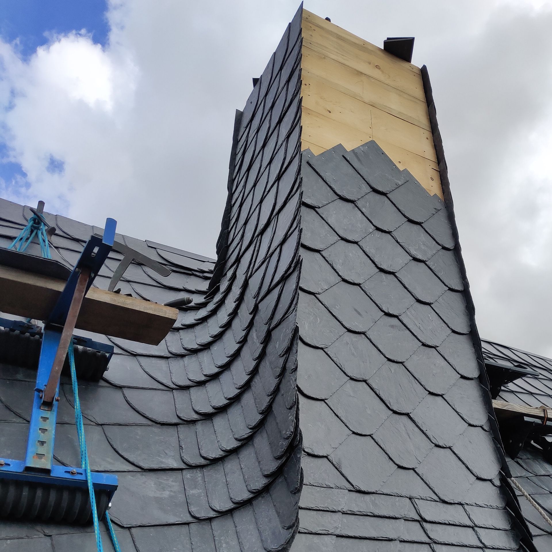 Ein Schornstein während der Schiefereindeckung, Kehldeckung. Grauer Schiefer überlappend.