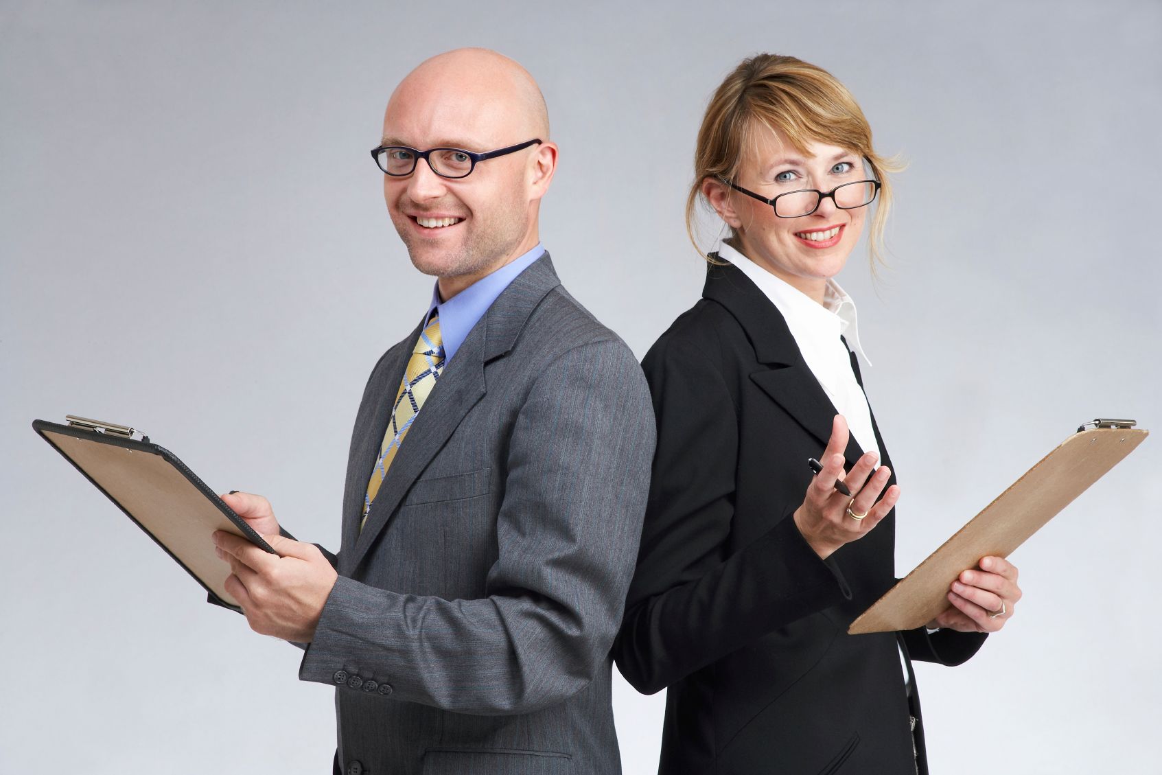 Bild von lächelndem Geschäftsmann und Geschäftsfrau, die beide einen Schreibblock in Händen halten Surgite Coaching Programme