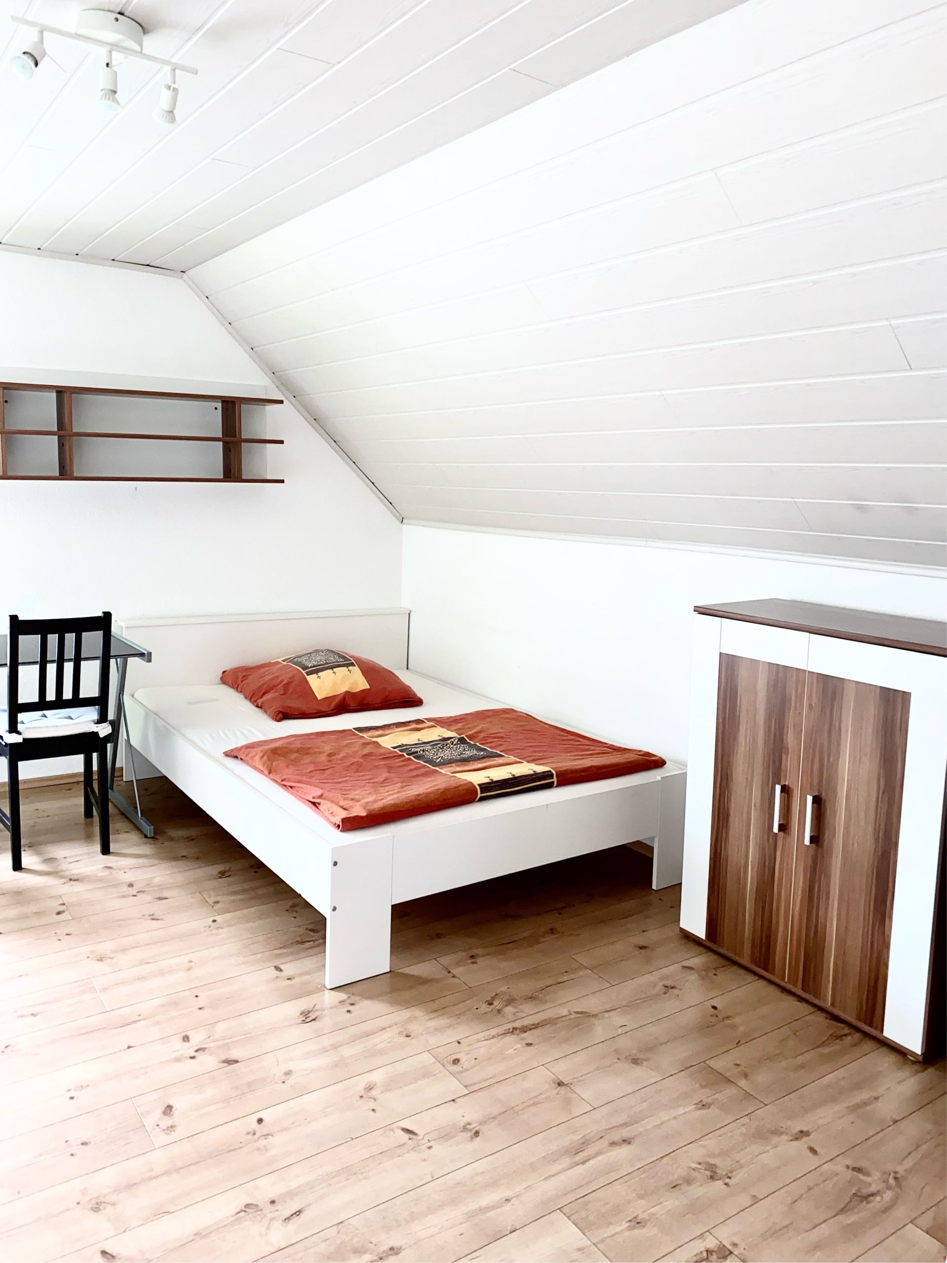 Möbliertes Einzelzimmer mit Bett, Schreibtisch, Kleiderschrank und TV.