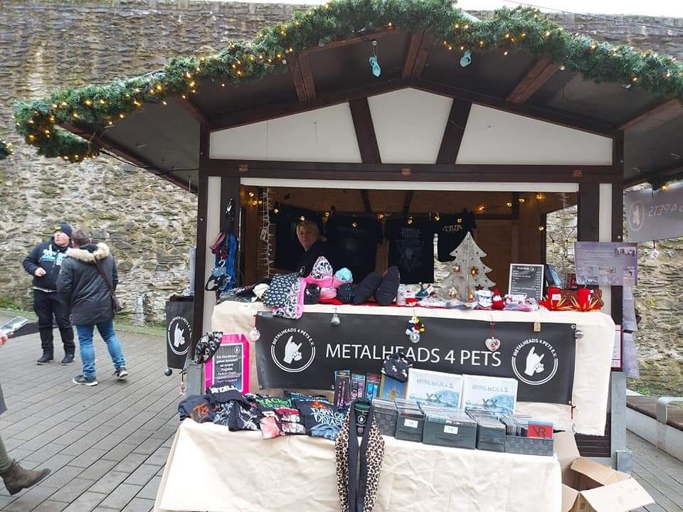 Verkaufsstand von Metalheads4Pets e.V. auf einem Markt mit Shirts, CDs und Spendenartikeln für den Tierschutz.